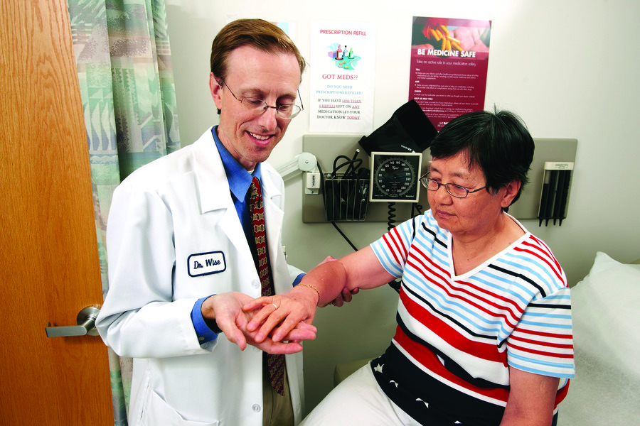 Doctor Bart Wise wearing white coat examining a patient’s hand