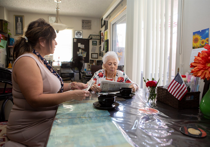 Latina caregiver sits at table with elderly mother for whom she cares