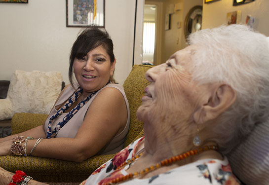 Latina caregiver looks lovingly at her elderly mom for whom she cares