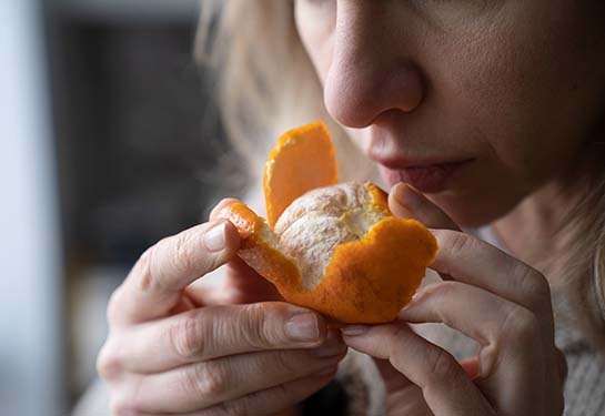 a woman holds a half-peeled mandarin close to her nose