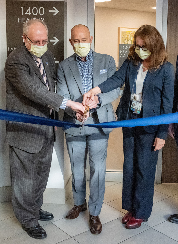 Stephen Cavanagh stands with David Lubarsky and Susan Murin outside the Healthy Aging Clinic holding scissors and cutting a blue ribbon.