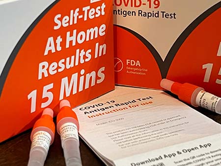 two orange ihealh COVID test kit boxes on a countertop with three vials of liquid and testing instructions