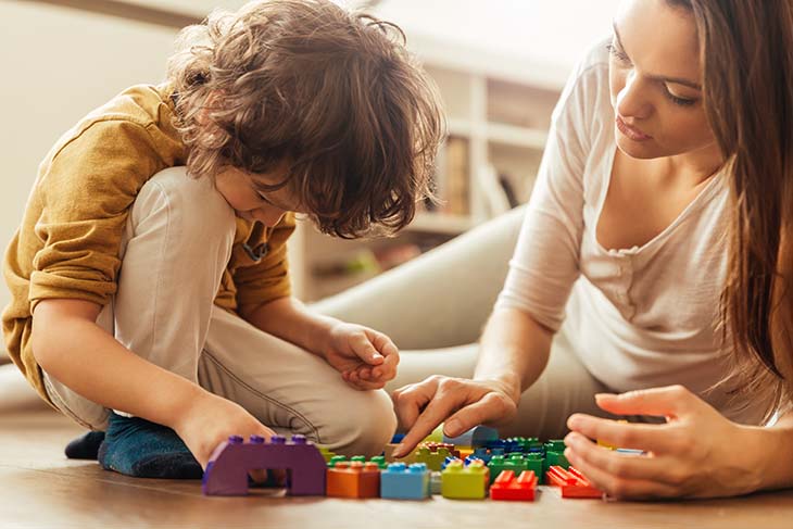 young boy playing with blocks next to his mom