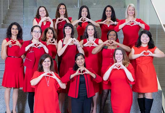 Female physicians wearing red dresses making a heart shape with their hands