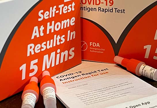 two orange ihealh COVID test kit boxes on a countertop with three vials of liquid and testing instructions