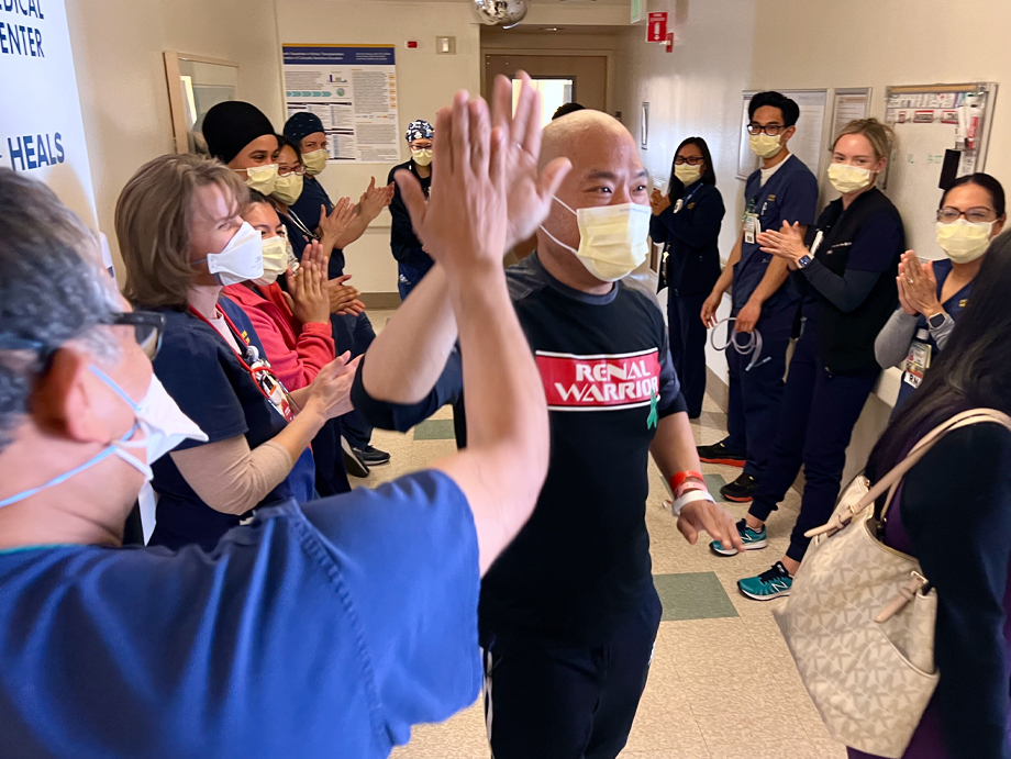 Wilson Du gives a 'high 5' to a nurse in scrubs while walking out of hospital surrounded by transplant team members lining the hallway