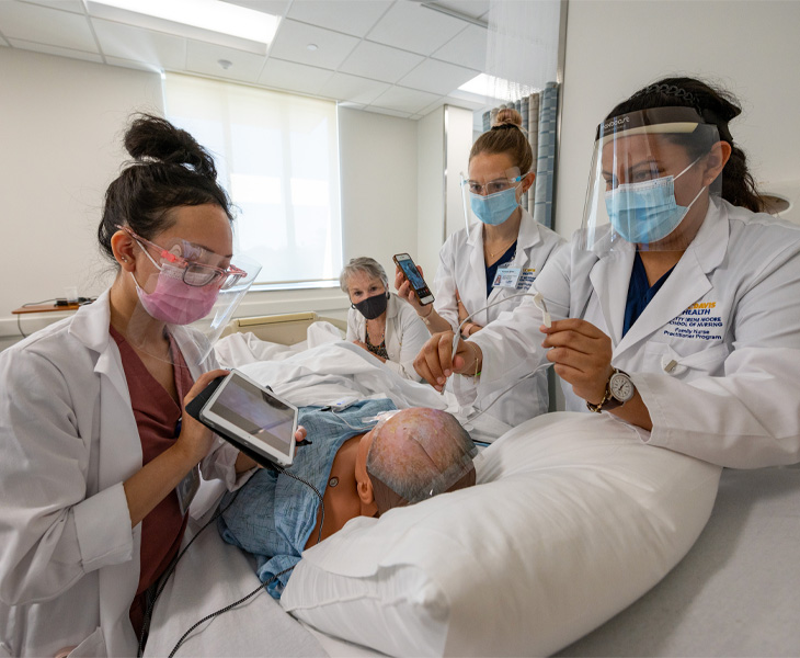 students wearing masks and face shields simulating care for manikin in hospital bed