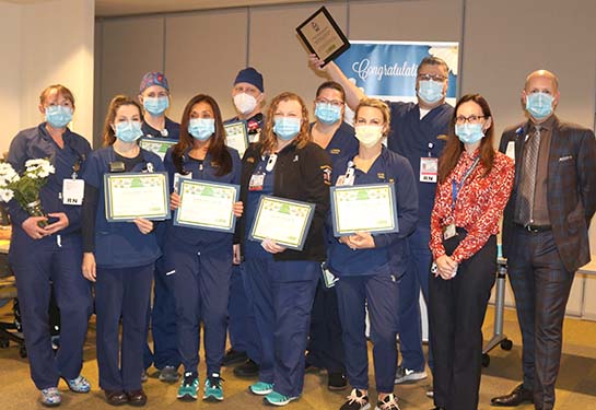 Nurses wearing blue scrubs holding certificates and wearing masks