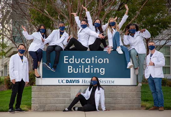 Medical students wearing masks and white coats with arms in the air