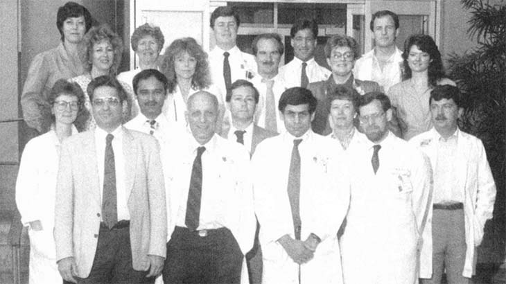 A black and white group photo from 1989 showing 20 people in business clothing and lab coats standing on stairs outside a building.  