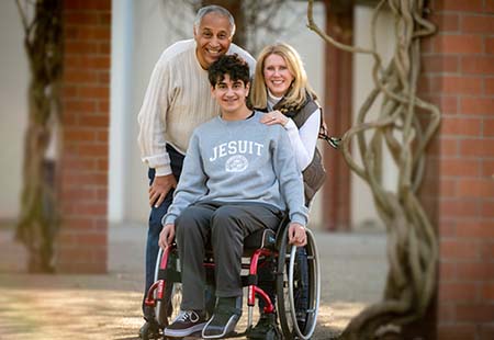 Bassem Mansour sitting in red wheelchair with mom and dad hugging his shoulders 