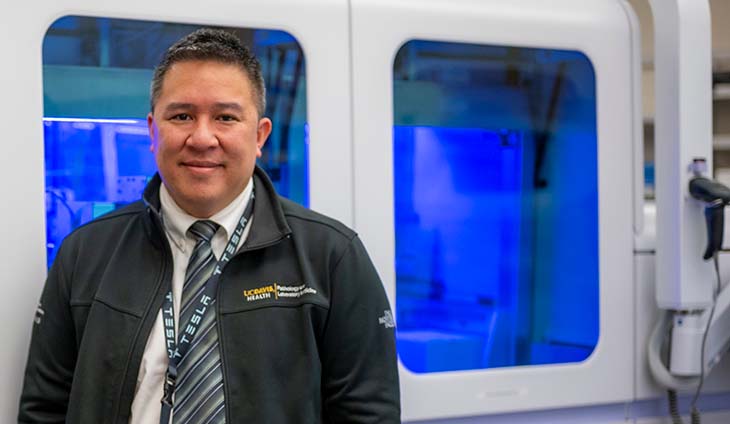 A man stands in front of a mechanized laboratory machine that processes medical samples.