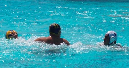 Man in a swimming pool holds a water polo ball in front of an opponent. 