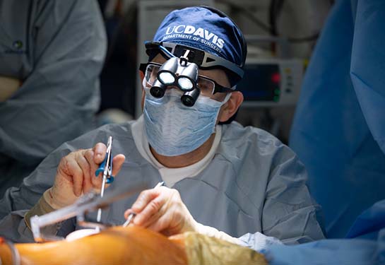 Surgeon wearing blue PPE performing surgery with UC Davis head cover