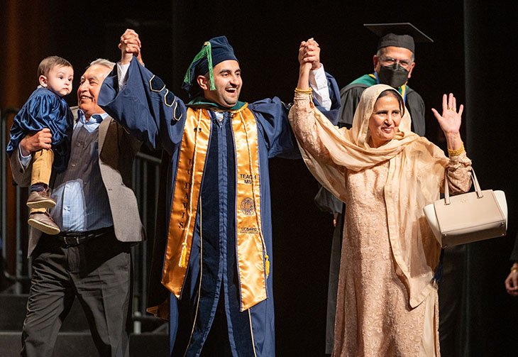 Bilawal Mahmood, wearing a blue graduation gown, with arms in the air accompanied by supporters to receive his medical school diploma