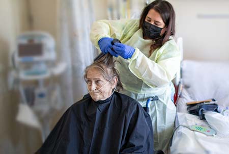 Hair stylist wearing PPE cutting hair of woman sitting in a wheelchair