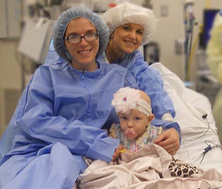 Female baby sitting on hospital bed with two adult females