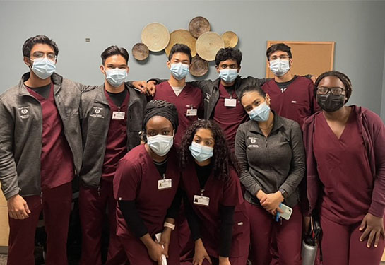 Nine undergraduate students from UC Davis wearing burgundy scrubs and cloth face masks pose for a picture at Imani Clinic