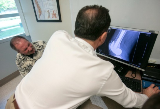 X-ray image on screen with doctor pointing at image as male patients listens