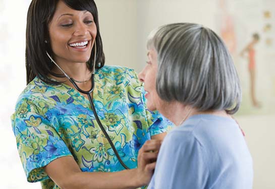 Nurse wearing scrubs listening to woman’s lungs with stethoscope