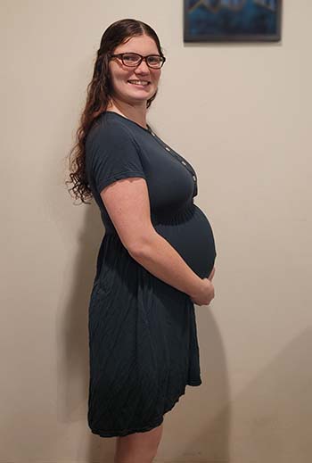 A pregnant woman stands sideways to show her baby bump. 