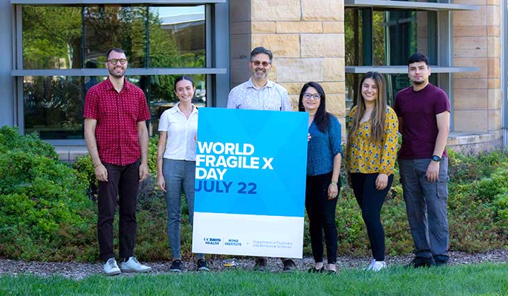David Hessl and his lab team – three men, three women, post in front of the MIND Institute with a sign that says “World Fragile X Day”