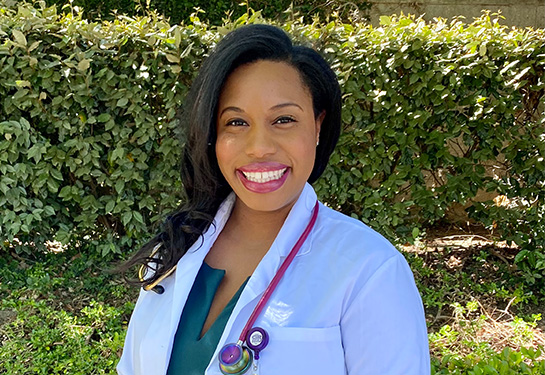 Elise Boykin-Harris wearing a white lab coat with green shrubs in the background