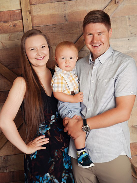 Family portrait of Nataliya Bahatyrevich standing with her husband while holding their toddler in between them