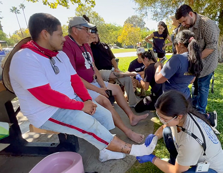 Six medical students provide foot care to three men at a picnic table after walking 15 miles during a march for farmworkers