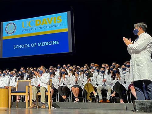 A new medical student gestures with pointed fingers to acknowledge the audience at Mondavi Center
