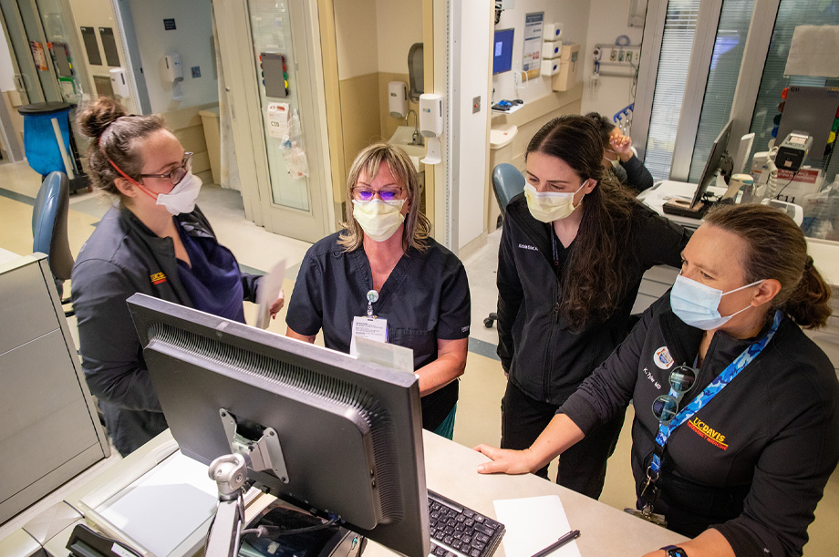 Katren Tyler, left, stands with three colleagues in front of computer in the ED; all wear masks