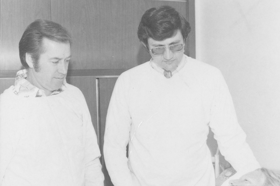 Cliff Haskell, left, stands next to doctor wearing white coat looking down on male burn patient lying in the bed