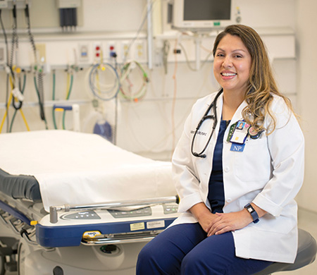 Sandra Calderon wears white coat and sits in clinic exam room