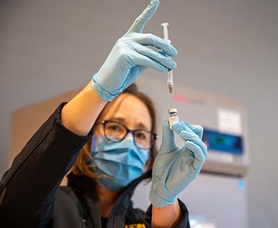 Woman wearing a blue mask drawing liquid out of a vile with a syringe