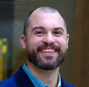 portrait of a younger man with brown hair, a beard and moustache, wearing a blue shirt. 