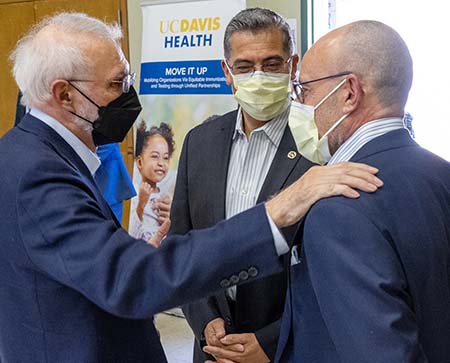 Three adult men wearing face masks gather in conversation 