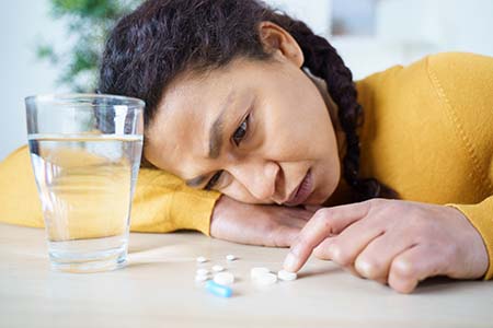 Sad woman looking at prescription pills next to a glass full of water. 