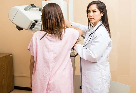La doctora está mirando una computadora mientras la paciente se hace una mamografía