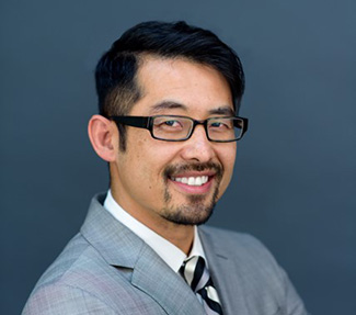 Asian male with short black hair and glasses, white shirt, black and white striped tie and gray blazer. 