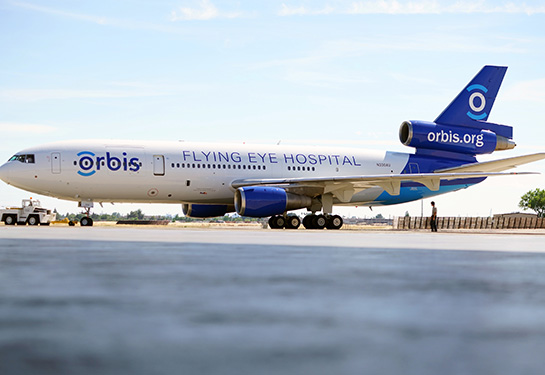 A white and blue plane with the words “Orbis” and “Flying Eye Hospital” is on an airport tarmac.
