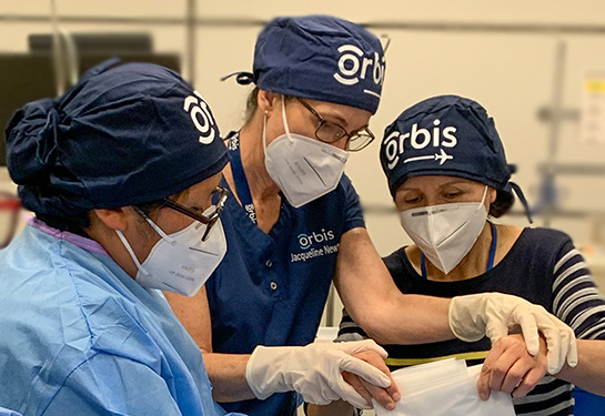 Three people with Orbis on their hats practicing surgical techniques