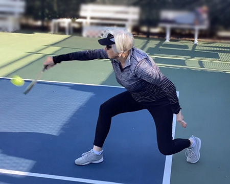 Cheryl Joordens playing pickleball and swinging racket low over the court.