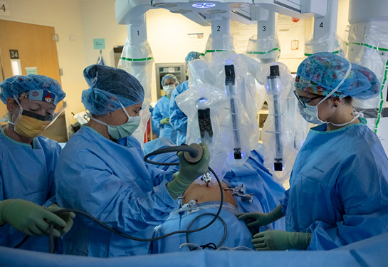Three surgeons standing in surgery room with robotic surgery machine