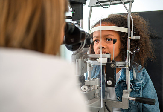 A Black girl is getting an eye examination from a female doctor.