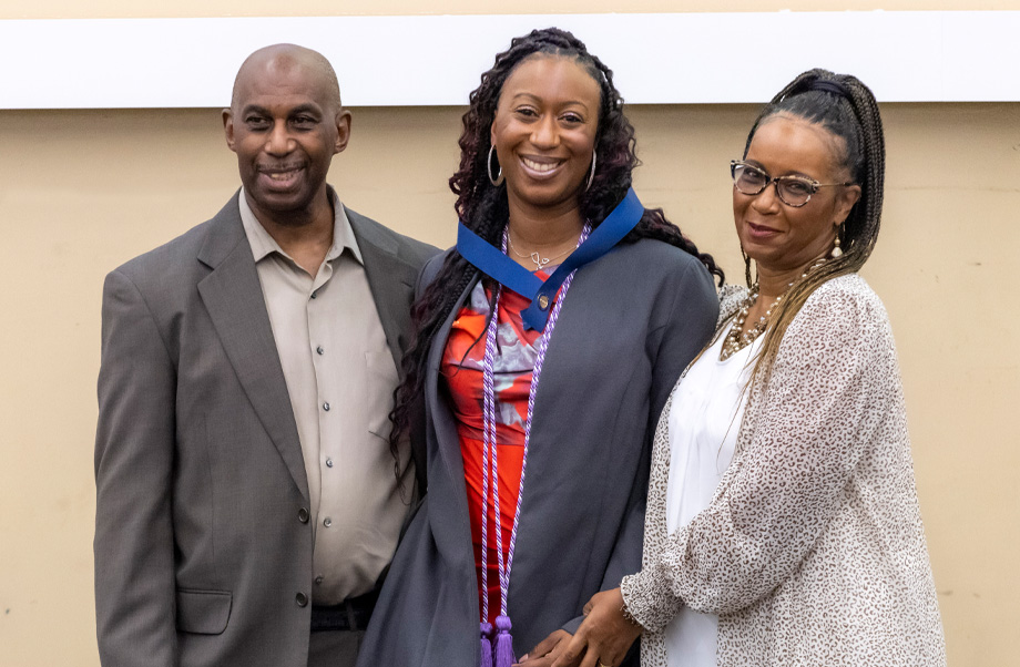 Jasmine Qualls, center, smiling and wearing pin on blue ribbon around her neck with her father standing to her left and her mother on her right