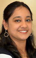 a woman with dark brown hair and gold dangling earrings smiles for the camera.