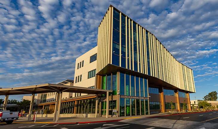 A four-story building with a striking curved and angular design against a blue sky with small white clouds. 