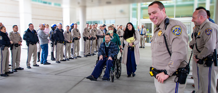 Aaron Weikert is pushed in a wheelchair surrounded by CHP officers