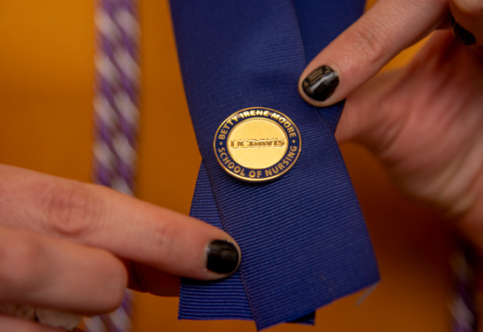 Female hands holding gold pin attached to blue ribbon
