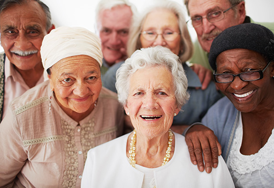 A diverse group of older people are gathered closely together and looking toward the camera and smiling.